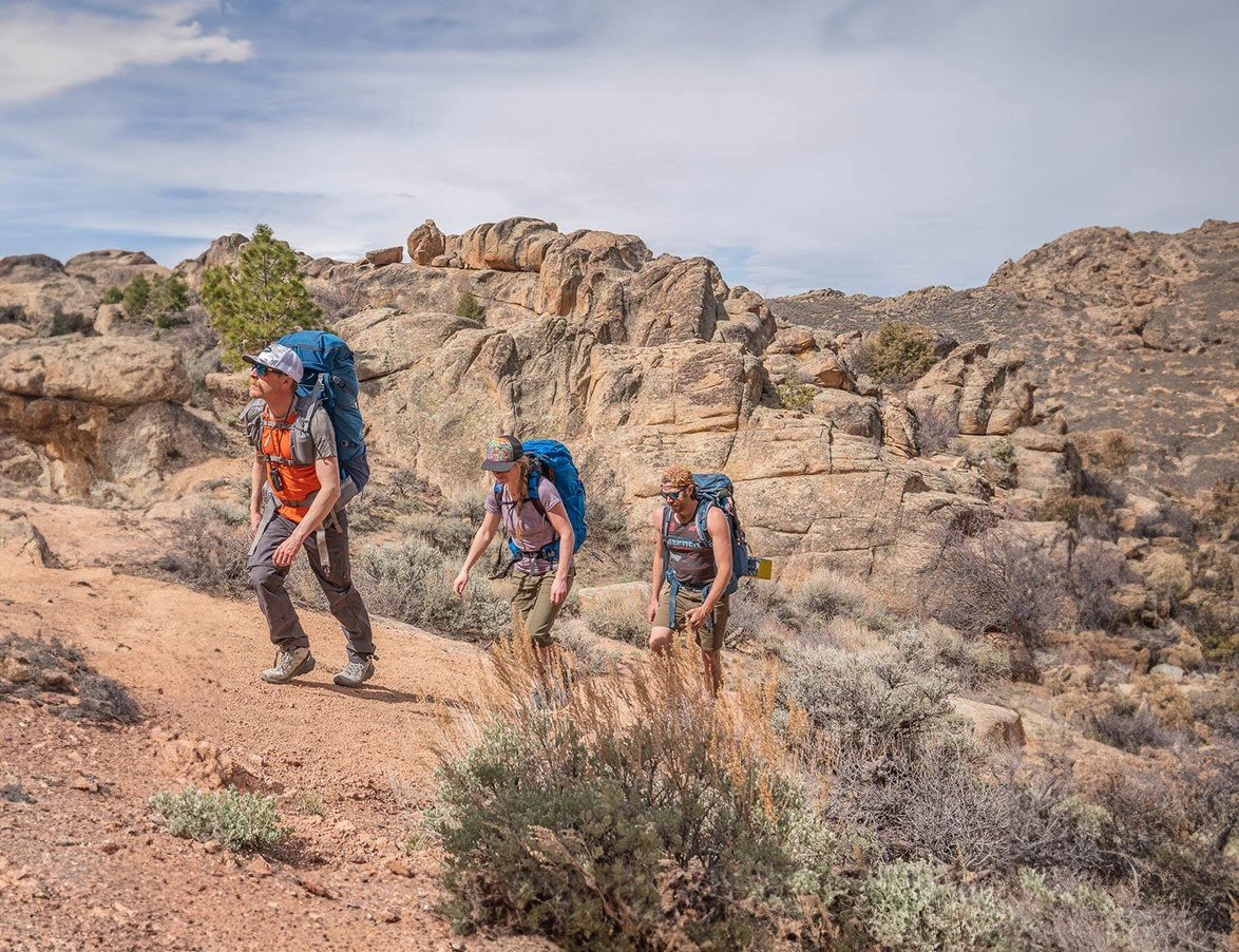 three hikers walking through arid landscape with backpacks