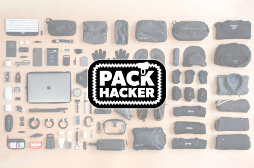 Travel gear laid out on a table, with a Pack Hacker logo overlay